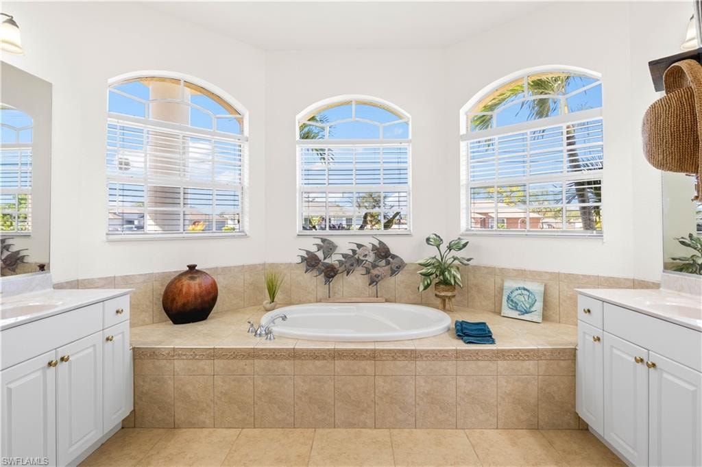 Full bath featuring two vanities, a garden tub, healthy amount of natural light, and light tile patterned floors
