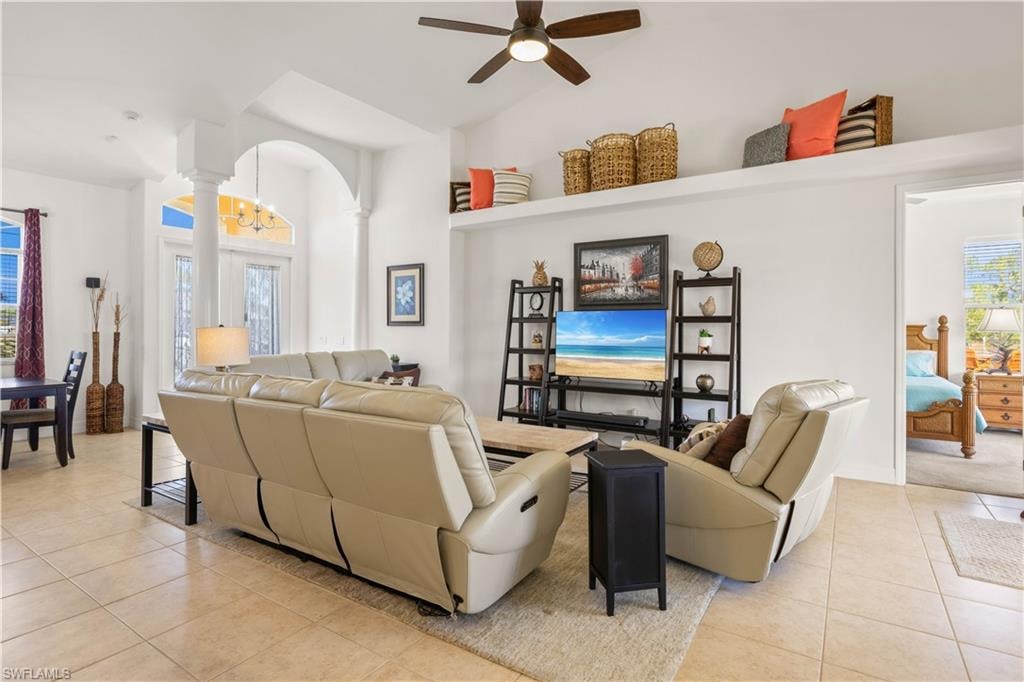 Living area with light tile patterned floors, a ceiling fan, high vaulted ceiling, arched walkways, and a chandelier