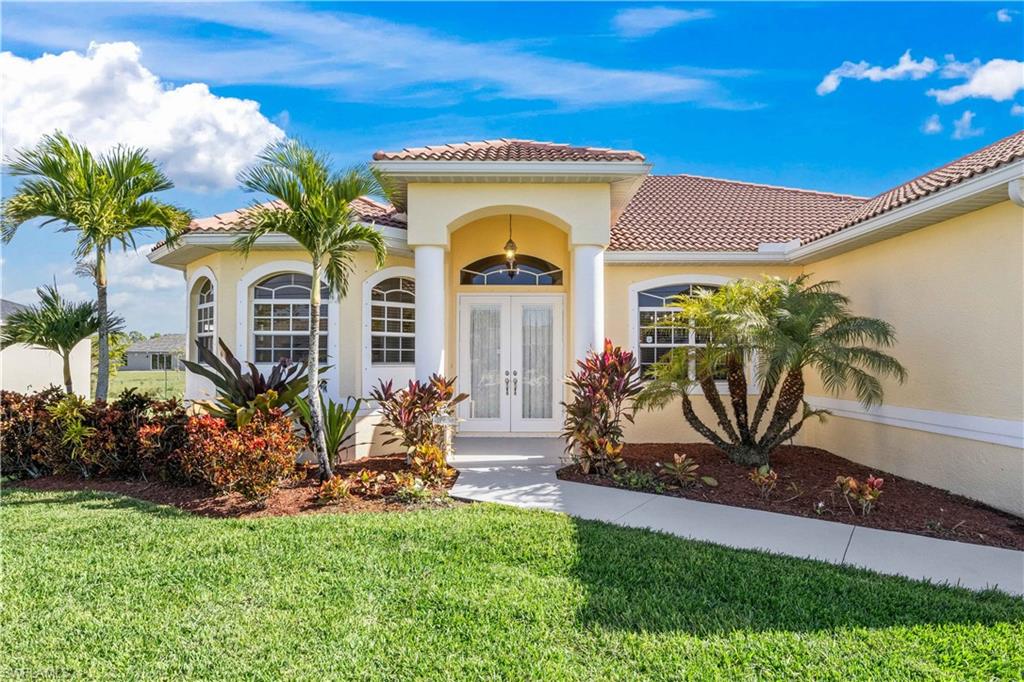 View of exterior entry with french doors, a tiled roof, a yard, and stucco siding