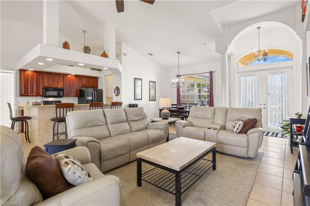 Living room with high vaulted ceiling, a chandelier, light tile patterned flooring, and a ceiling fan