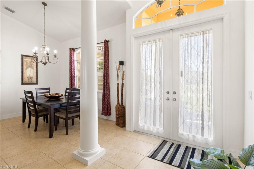 Foyer with a chandelier, french doors, ornate columns, lofted ceiling, and light tile patterned flooring