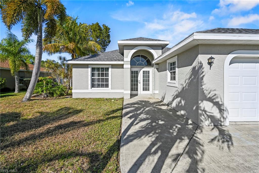 Ranch-style home featuring a front lawn, roof with shingles, stucco siding, and driveway
