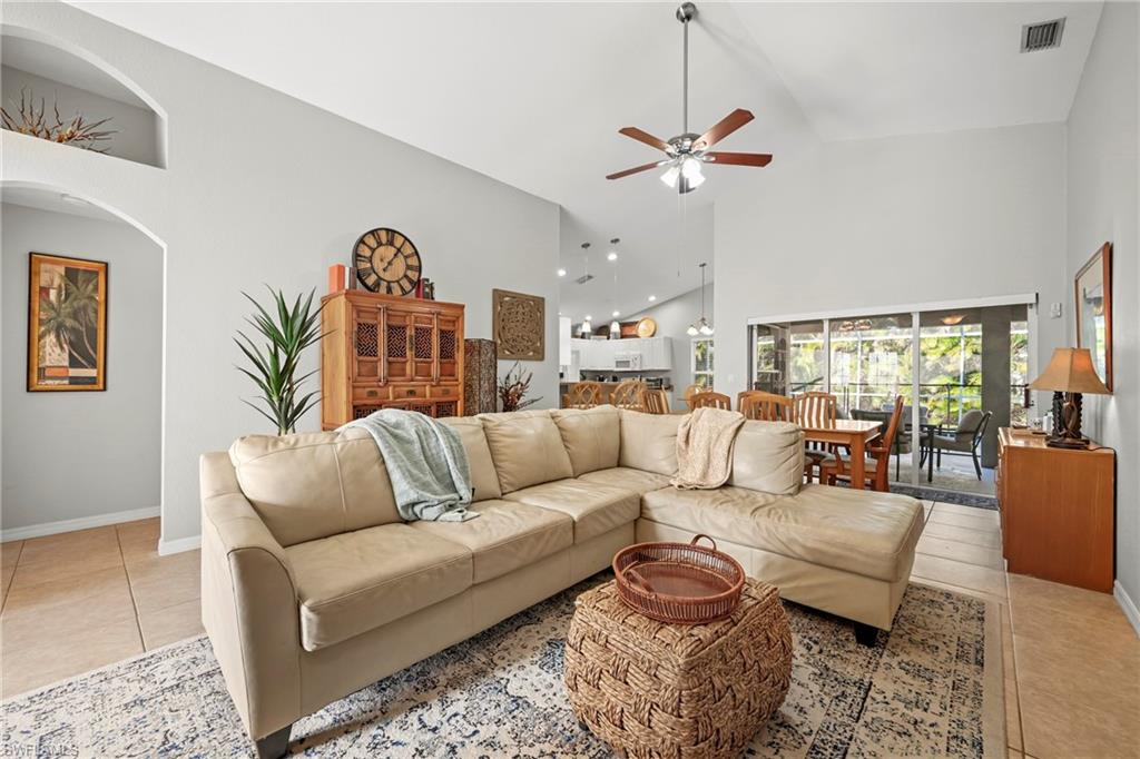 Living room featuring light tile patterned flooring, high vaulted ceiling, ceiling fan, and arched walkways