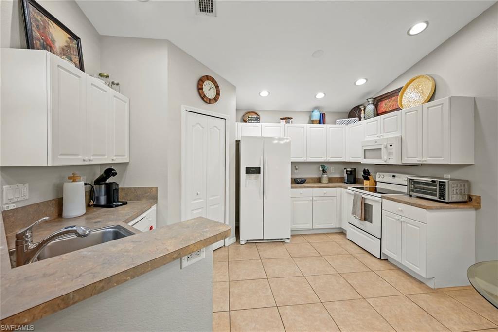 Kitchen featuring a kitchen bar, white appliances, hanging light fixtures, a peninsula, and white cabinetry