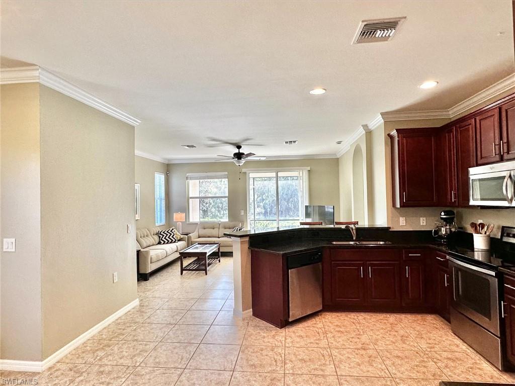 Kitchen with appliances with stainless steel finishes, ornamental molding, open floor plan, a ceiling fan, and light tile patterned floors