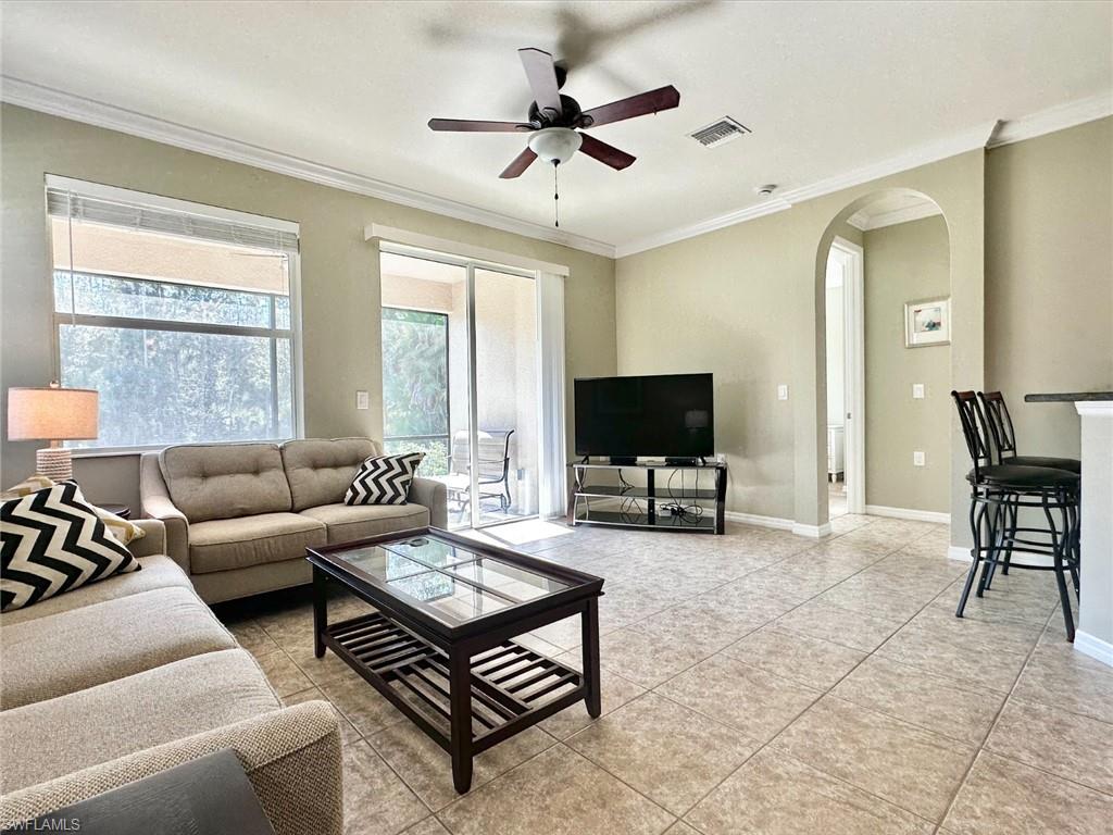 Living area with crown molding, arched walkways, a ceiling fan, and light tile patterned floors