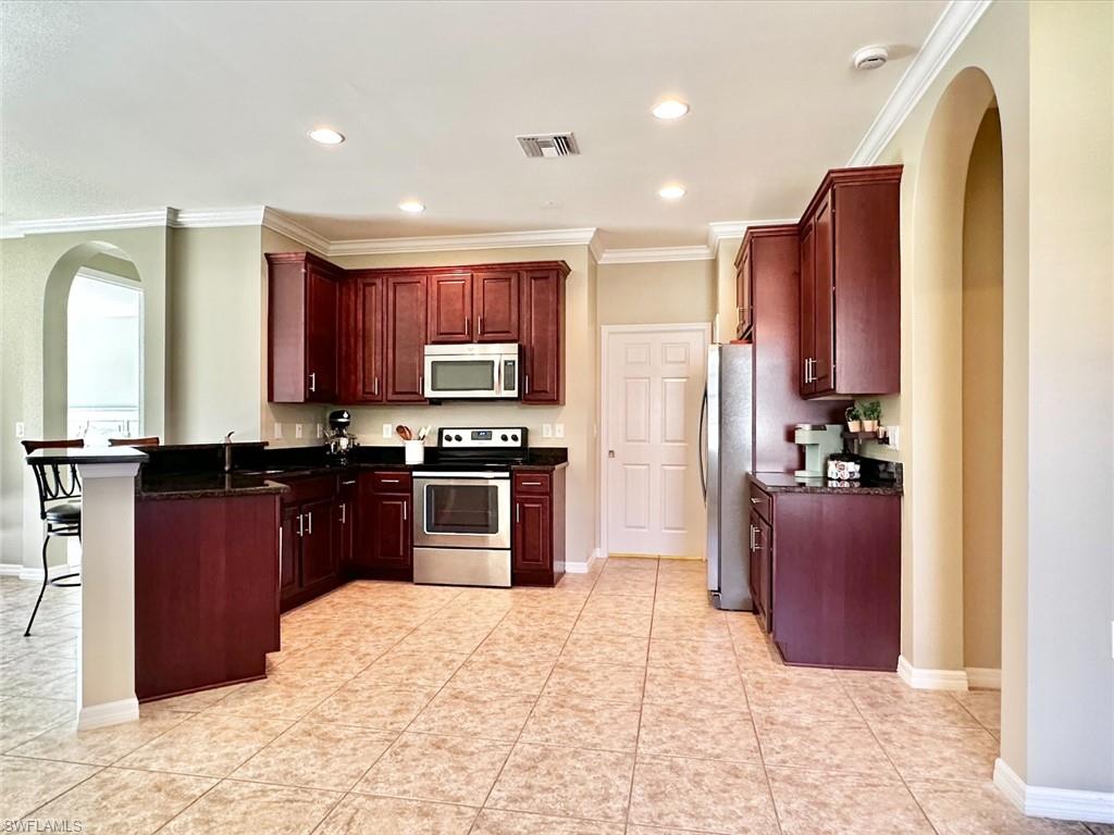 Kitchen with arched walkways, dark brown cabinets, stainless steel appliances, ornamental molding, and dark stone counters