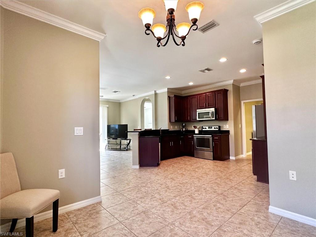 Kitchen featuring dark countertops, ornamental molding, appliances with stainless steel finishes, arched walkways, and a peninsula