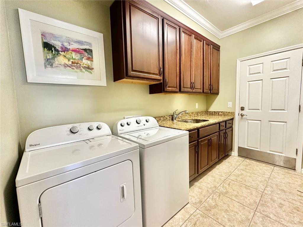 Laundry room featuring crown molding, cabinet space, washing machine and clothes dryer, and light tile patterned floors