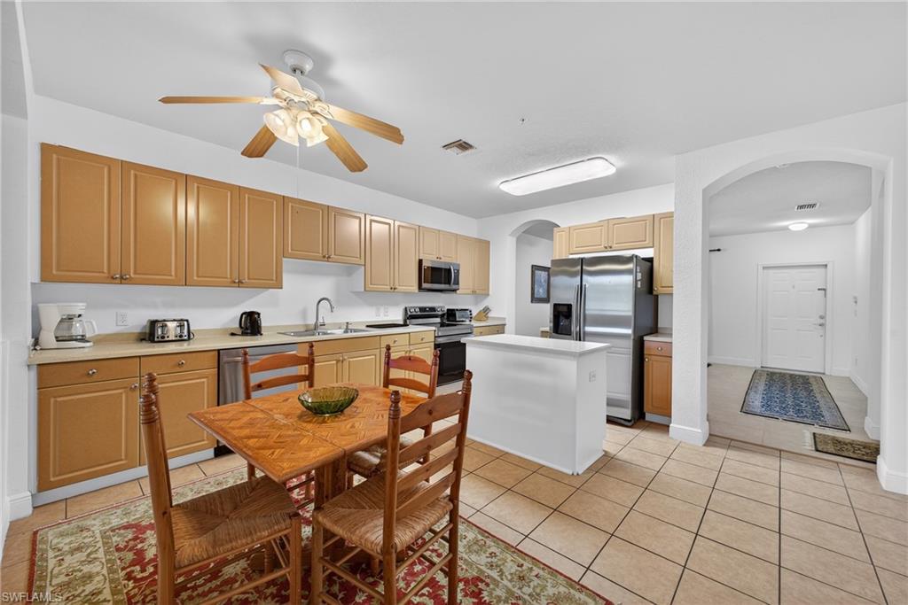 Kitchen featuring arched walkways, light tile patterned floors, light countertops, stainless steel appliances, and a kitchen island