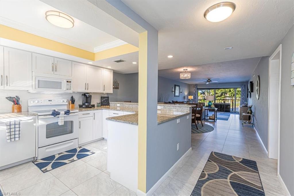 Kitchen featuring white appliances, light stone countertops, a ceiling fan, white cabinetry, and a peninsula