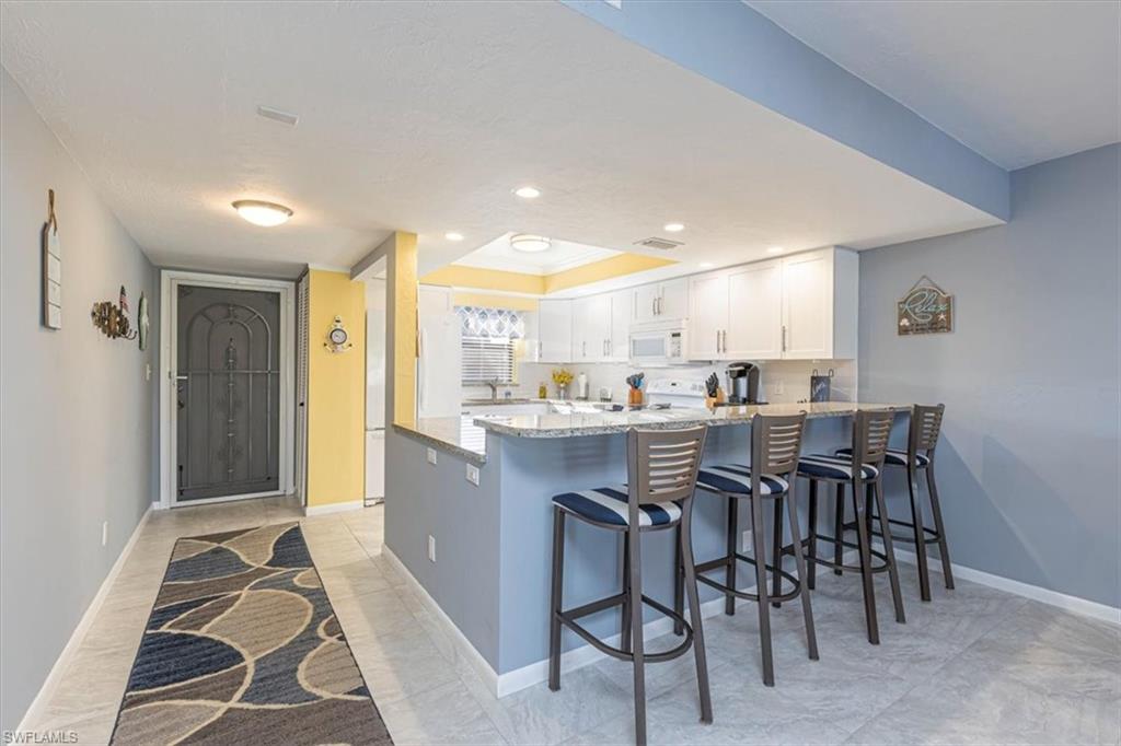 Kitchen featuring a kitchen bar, light stone countertops, white cabinetry, a peninsula, and white appliances