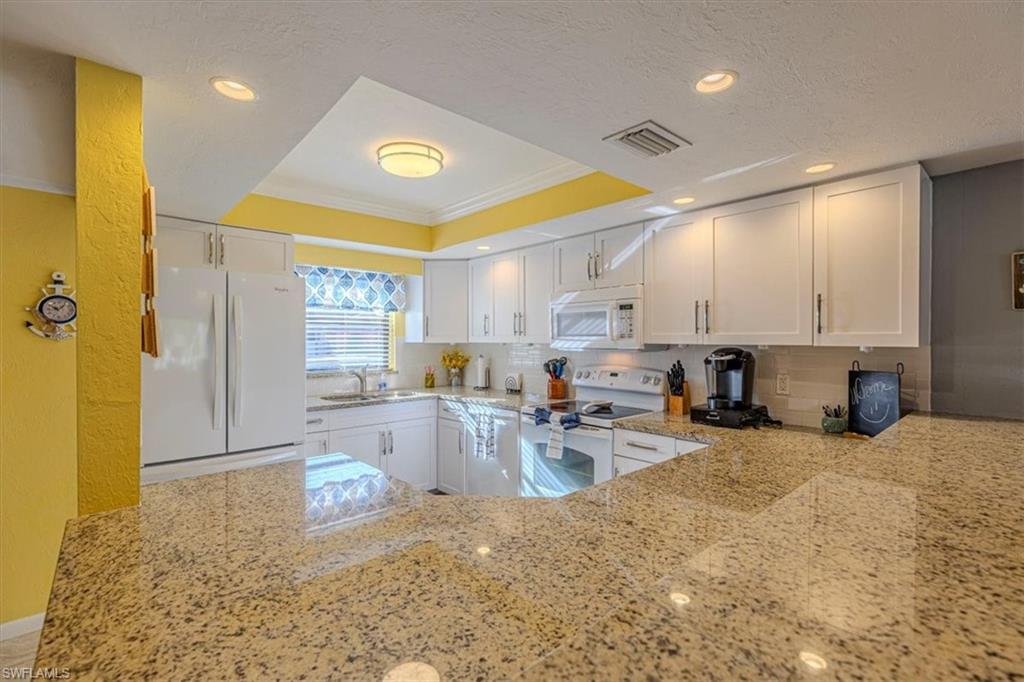 Kitchen with light stone countertops, white appliances, white cabinets, a tray ceiling, and backsplash