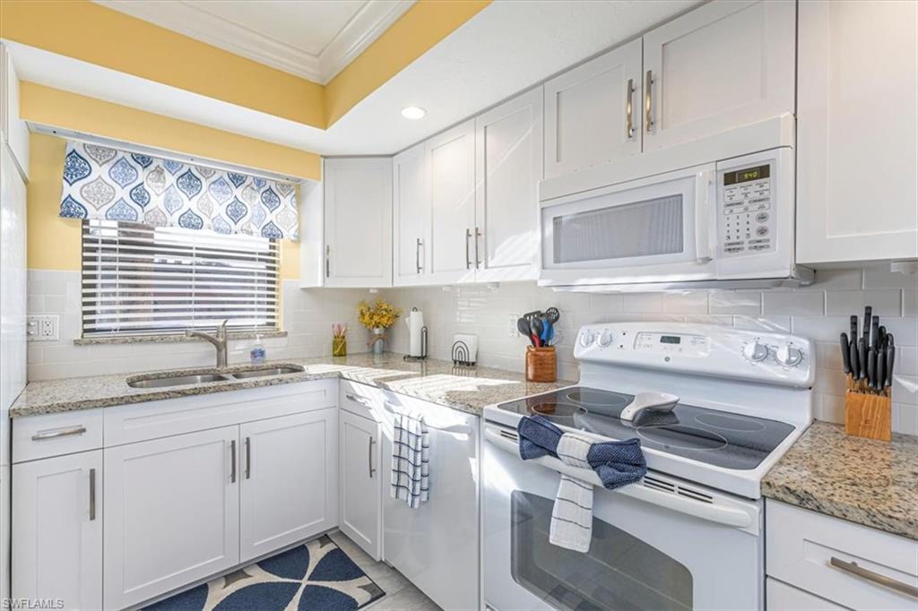 Kitchen with white appliances, white cabinetry, crown molding, light stone counters, and backsplash
