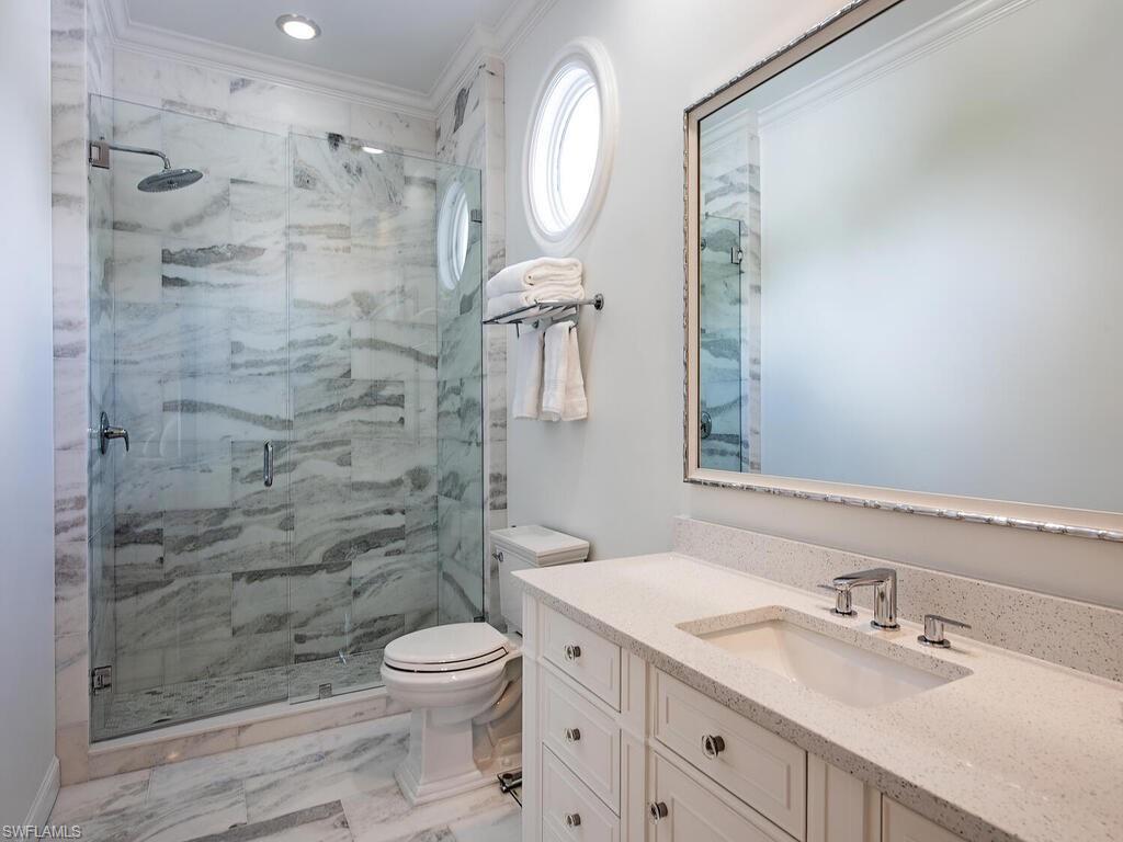 Full bath with vanity, light marble finish flooring, a marble finish shower, and ornamental molding