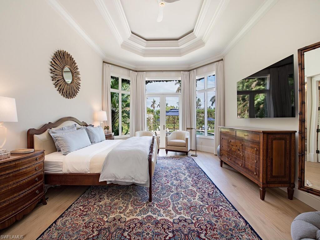 Bedroom with a tray ceiling, wood finished floors, crown molding, french doors, and a ceiling fan