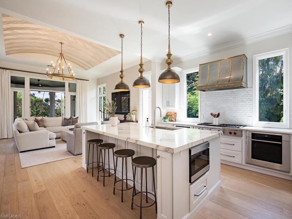 Kitchen featuring decorative light fixtures, a kitchen island with sink, light stone countertops, light wood finished floors, and crown molding