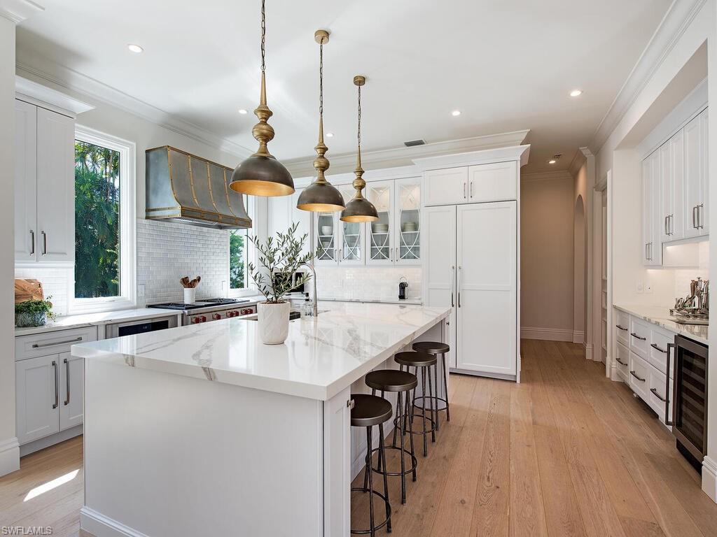 Kitchen featuring a breakfast bar area, white cabinets, ornamental molding, decorative light fixtures, and wall chimney exhaust hood