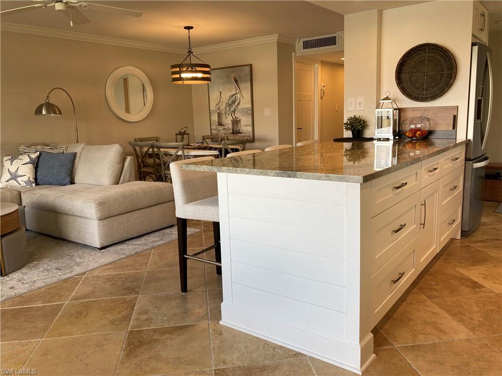 Kitchen featuring a kitchen breakfast bar, dark stone counters, white cabinetry, ornamental molding, and stainless steel fridge