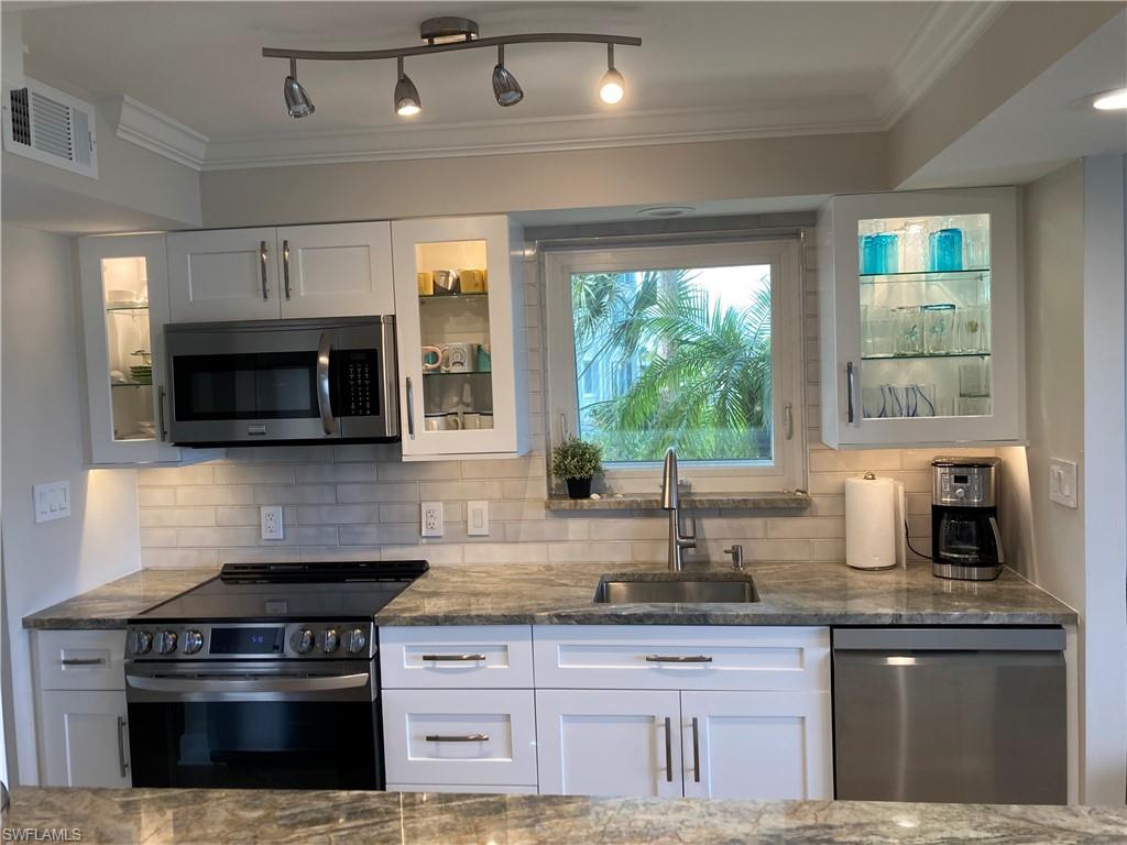 Kitchen featuring glass insert cabinets, appliances with stainless steel finishes, white cabinets, tasteful backsplash, and ornamental molding