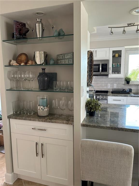 Bar with white cabinetry, open shelves, dark stone countertops, crown molding, and backsplash