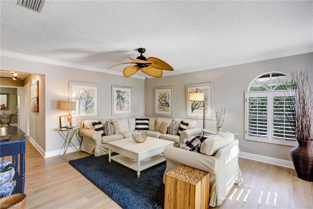 Living room with crown molding, a textured ceiling, ceiling fan, and light wood-type flooring