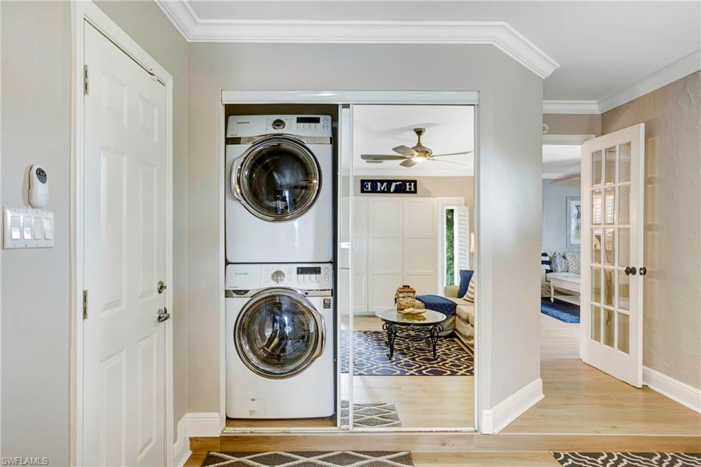 Clothes washing area with wood-type flooring, ornamental molding, french doors, and stacked washer / dryer