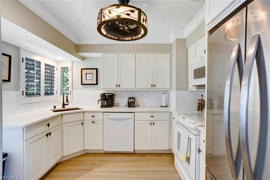 Kitchen with sink, white cabinets, crown molding, white appliances, and light hardwood / wood-style flooring