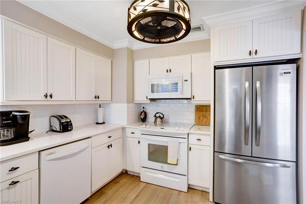 Kitchen featuring white cabinetry, backsplash, white appliances, and ornamental molding