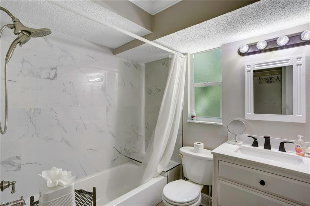 Full bathroom featuring vanity, toilet, shower / bath combo with shower curtain, and a textured ceiling