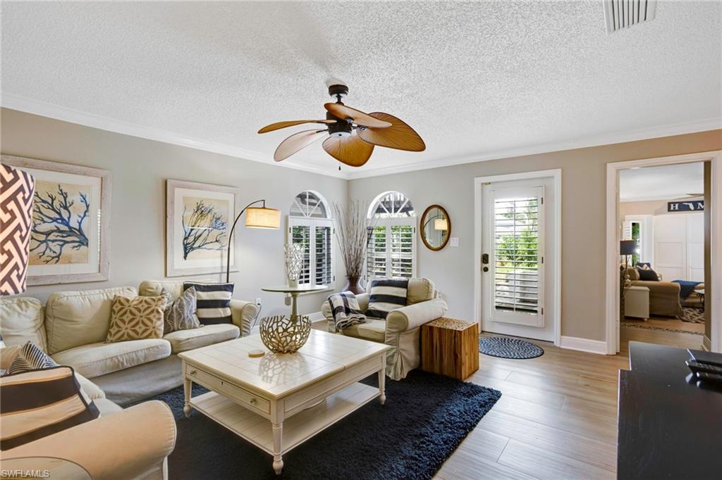 Living room with crown molding, ceiling fan, a textured ceiling, and light wood-type flooring
