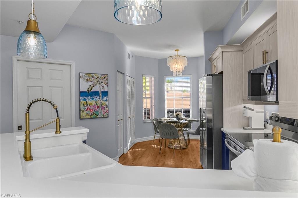 Kitchen with stainless steel appliances, pendant lighting, light wood finished floors, and a chandelier