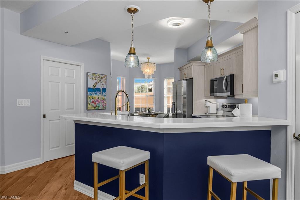 Kitchen with pendant lighting, a kitchen bar, stainless steel appliances, light wood-style floors, and a chandelier