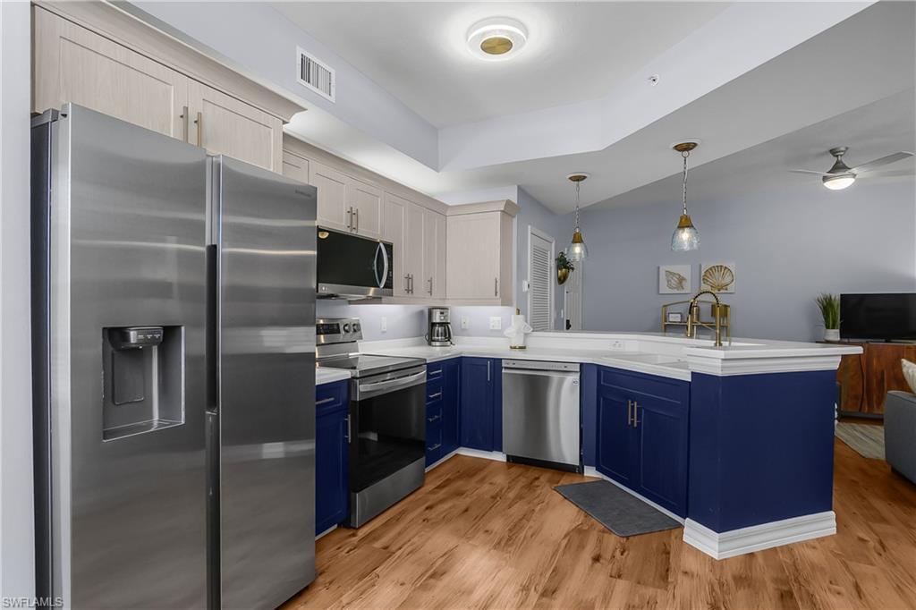 Kitchen with appliances with stainless steel finishes, blue cabinets, pendant lighting, open floor plan, and a peninsula