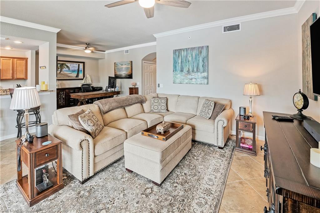 Living room featuring ceiling fan, light tile patterned flooring, and crown molding