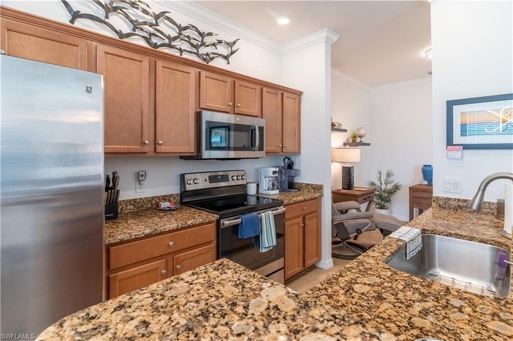 Kitchen with appliances with stainless steel finishes, brown cabinetry, light stone countertops, and crown molding
