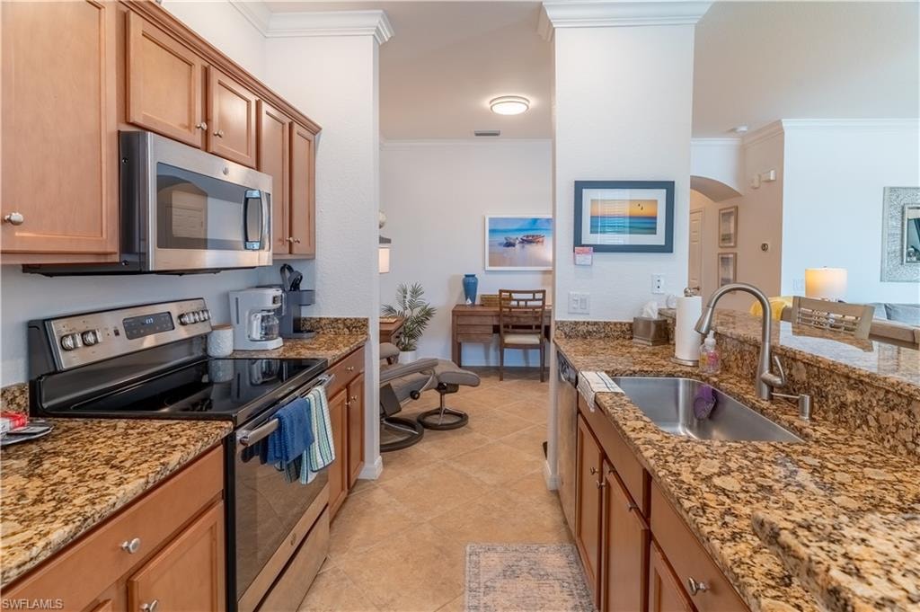Kitchen featuring stainless steel appliances, light stone counters, ornamental molding, arched walkways, and light tile patterned floors