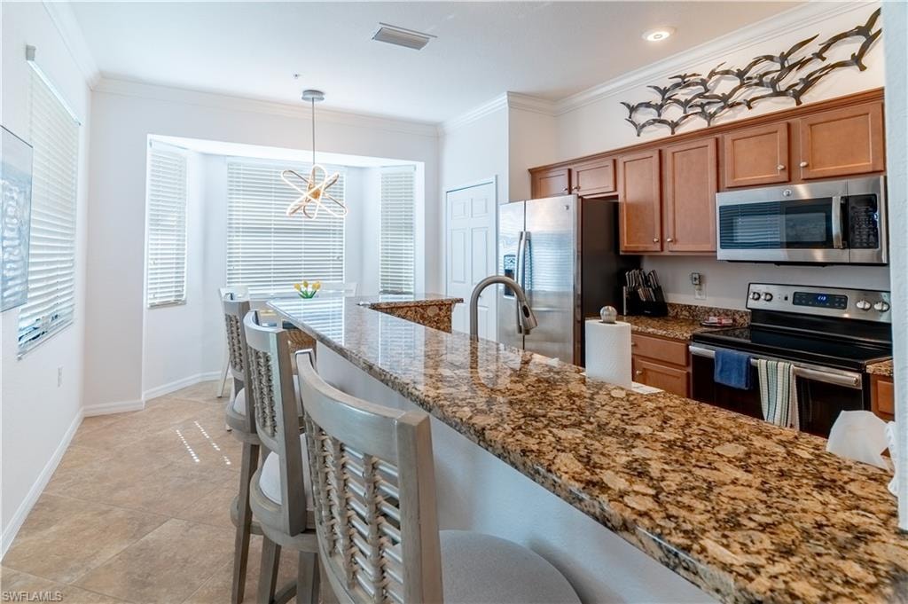 Kitchen with appliances with stainless steel finishes, brown cabinetry, dark stone countertops, a breakfast bar, and ornamental molding