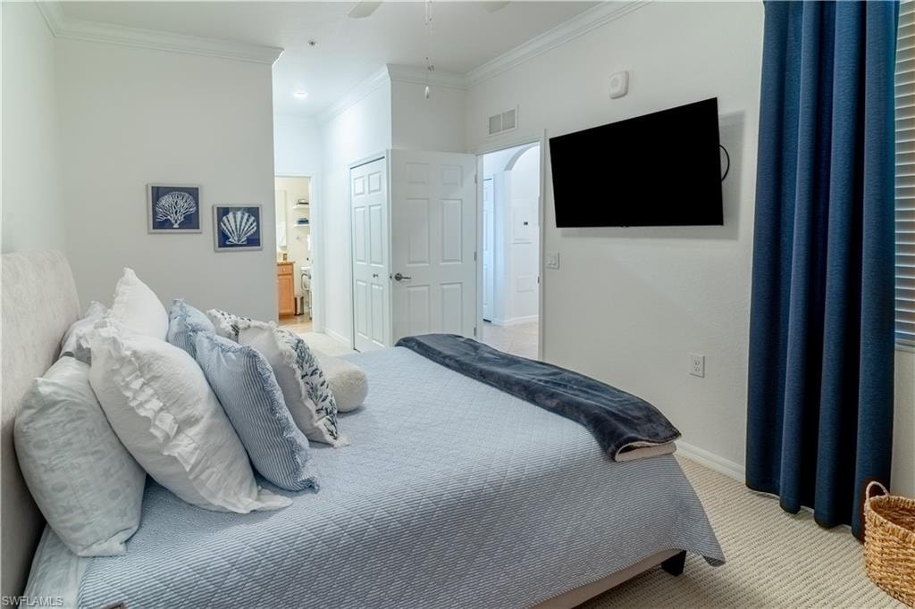 Bedroom featuring carpet flooring, crown molding, ensuite bath, a ceiling fan, and a closet