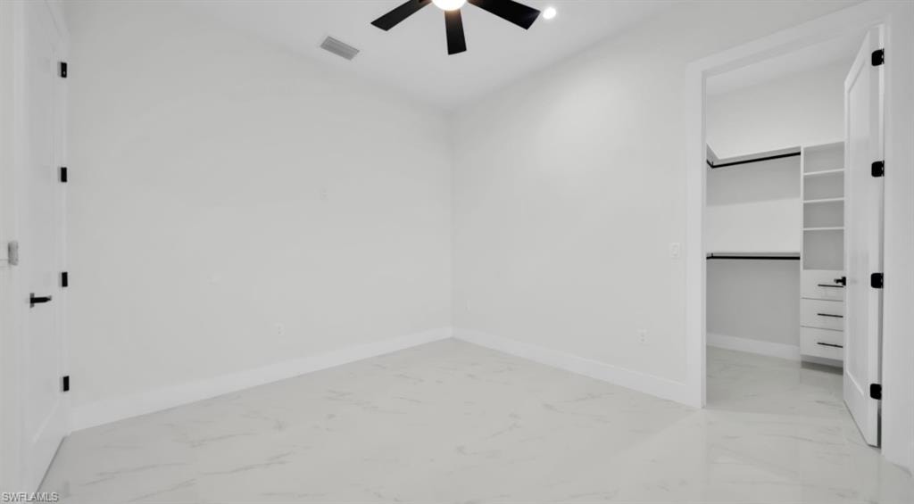 Unfurnished bedroom featuring a walk in closet, light marble finish floors, and a ceiling fan