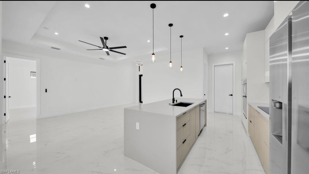 Kitchen featuring modern cabinets, appliances with stainless steel finishes, recessed lighting, decorative light fixtures, and light stone countertops