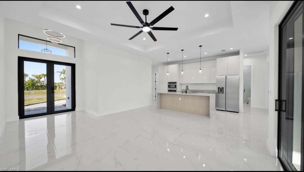 Kitchen featuring open floor plan, stainless steel fridge, a tray ceiling, a center island with sink, and recessed lighting