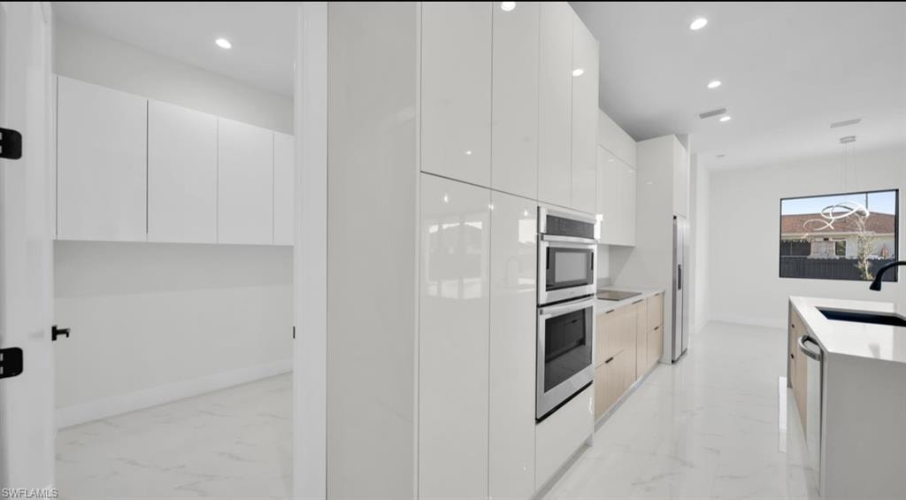 Kitchen featuring modern cabinets, light marble finish floors, white cabinetry, and recessed lighting