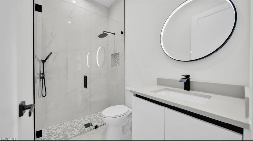 Bathroom with vanity, a marble finish shower, and marble look tile flooring
