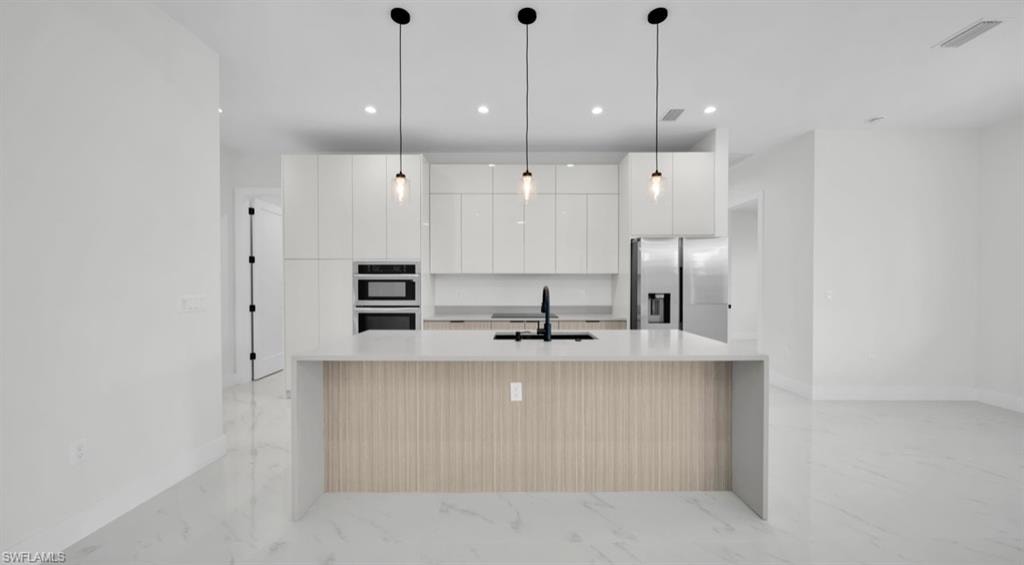 Kitchen featuring modern cabinets, decorative light fixtures, light stone counters, stainless steel appliances, and white cabinets