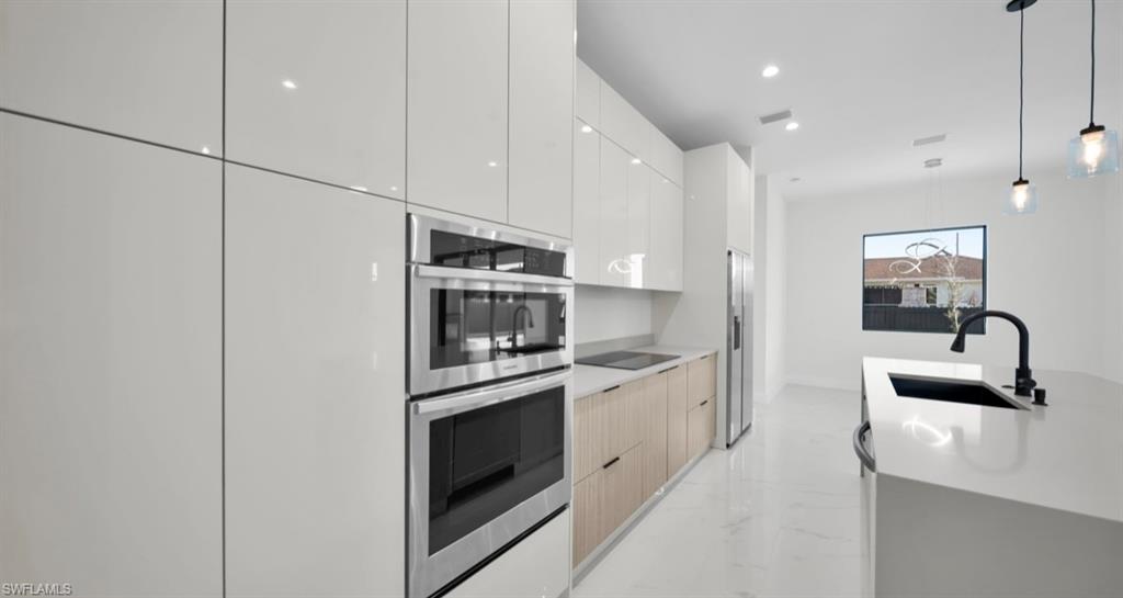 Kitchen featuring decorative light fixtures, modern cabinets, light marble finish floors, stainless steel appliances, and recessed lighting