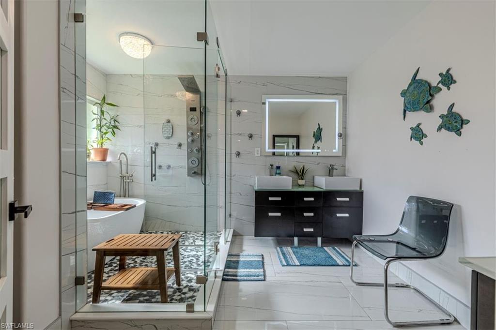 Full bath with double vanity, a marble finish shower, a freestanding tub, and tile walls
