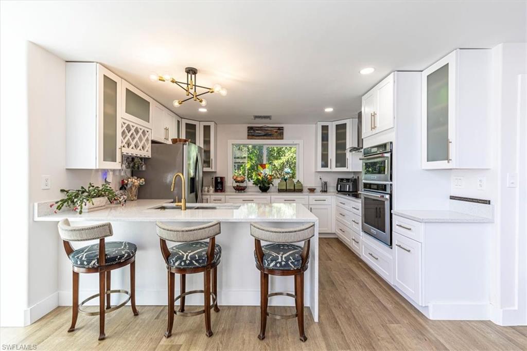 Kitchen featuring glass insert cabinets, a kitchen bar, white cabinetry, recessed lighting, and light stone countertops
