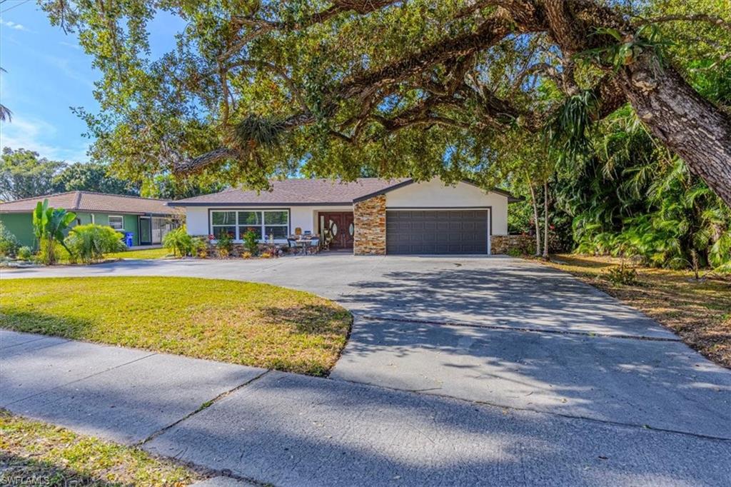 Single story home featuring asphalt driveway, stucco siding, stone siding, a garage, and a front yard