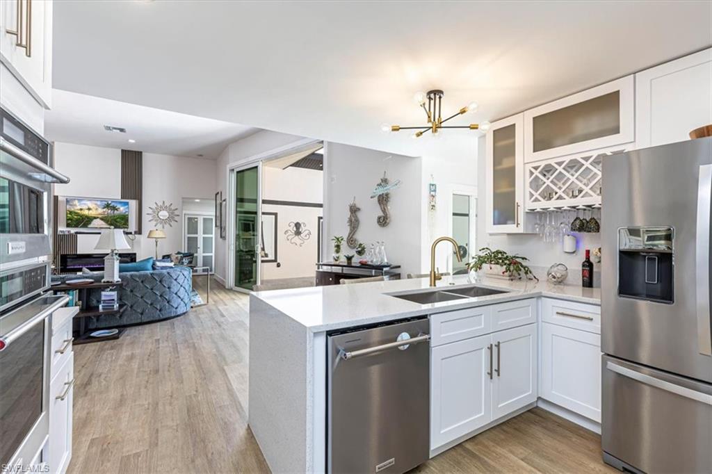 Kitchen featuring stainless steel appliances, white cabinets, light stone counters, a chandelier, and a peninsula